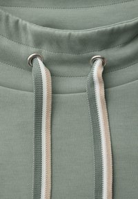 Sweatshirt met capuchon in gedempt groen stof, voorzien van zilveren oogjes en trekkoorden met een gestructureerd, crèmekleurig en lichtgroen accent.