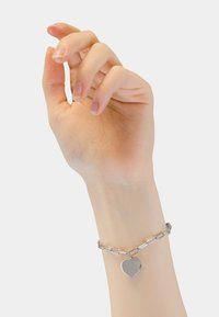 Zilveren schakelarmband met ovale schakels en een gepolijste harthanger. De hand is elegant gepositioneerd, waardoor het ontwerp van de armband goed zichtbaar is.