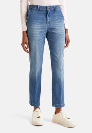 Personne portant un jean droit bleu clair avec des détails délavés et des baskets blanches sur fond blanc.