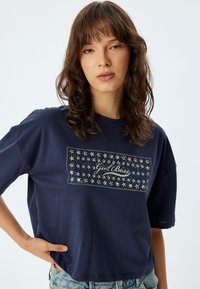 Camiseta azul marino hecha de una tela suave, con un gran estampado de estrellas y el texto "Girl Boss" en plata. Manga corta y corte relajado.