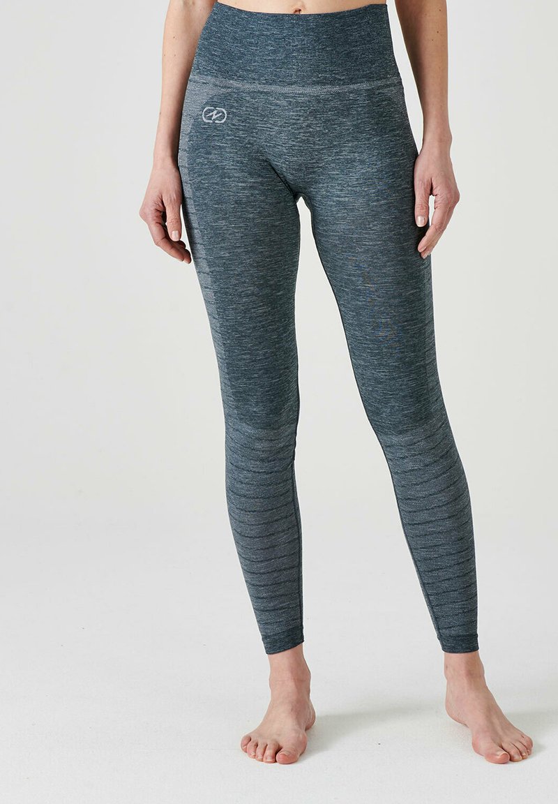 Femme portant des leggings taille haute sans coutures gris foncé, debout pieds nus sur un fond clair.