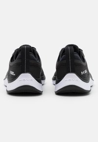 Svarta träningsskor med ovandel i nät, vit sula och grå accent. Har en hälöglan och "HOVR"-logotyp på mellansulan.