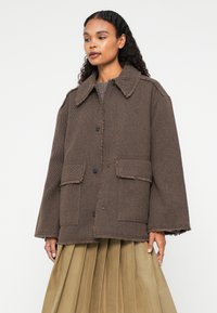 Bruine herringbonejas met een klassieke kraag, knoopsluiting en twee vozakken. Gerafelde randen en een ontspannen pasvorm.