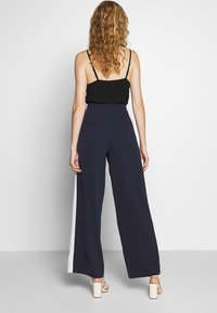 Marinblå vida byxor med vita sidopaneler, hög midja och slät textur. Bärs med en svart topp och vita blockklack-sandelar.