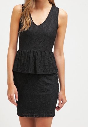 Robe noire sans manches en dentelle avec encolure en V et taille à volant, jupe ajustée, portée par un mannequin féminin debout sur un fond uni.