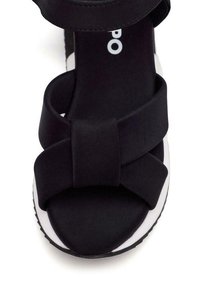 Sanda negra con un gran lazo de tela en la parte delantera, textura suave, entresuela blanca y un diseño de suela robusta.