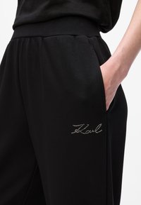 Melni sporta bikses ar elastīgu jostu, sānu kabatām un izšūtu logotipu ar rhinestone akmeņiem kreisajā augšstilbā. Izgatavotas no mīksta materiāla.
