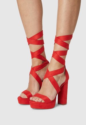 Sandales à plateforme à talons hauts en daim rouge avec des lanières croisées autour des chevilles et des orteils ouverts, présentant un talon carré épais.