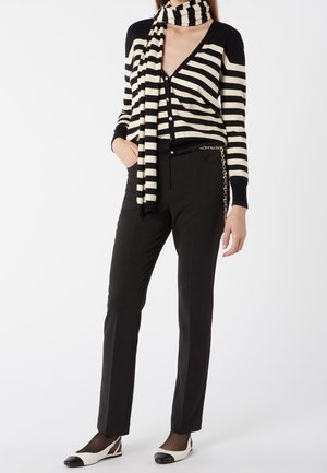 Schwarz- und cremegestreifter Cardigan mit Knöpfen, kombiniert mit maßgeschneiderten schwarzen Hosen und zweifarbigen Schuhen. Schal um den Hals drapiert.