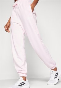 Ljusrosa sweatpants med elastisk midja, dragsko, sidofickor och vit logodetalj. Manschetterna är åtsittande vid anklarna.