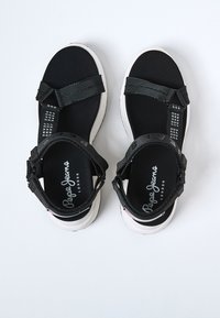 Svarta sandaler med justerbara remmar, vadderad svart fotbädd och vit gummisula. Har "Pepe Jeans London"-logotyp på innersulan.