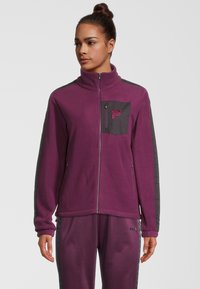 Chaqueta de forro polar morado con cuello alto, cremallera frontal y paneles de contraste en gris. Cuenta con un bolsillo en el pecho y puños elásticos.