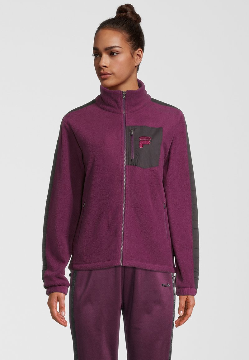 Chaqueta de forro polar morado con cuello alto, cremallera frontal y paneles de contraste en gris. Cuenta con un bolsillo en el pecho y puños elásticos.
