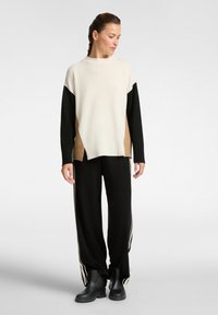 Sweter dzianinowy w kolorze ecru, czarnym i beżowym o luźnym kroju. W komplecie z czarnymi, luźnymi spodniami z bocznymi paskami i masywnymi czarnymi botkami.