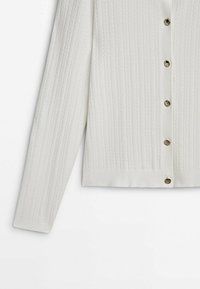 Cardigan blanc en maille avec manches longues et cinq boutons en écaille disposés sur le devant au centre.