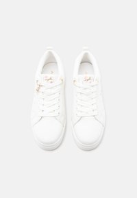 Baskets blanches à lacets, ornées de décorations dorées en forme de cheval et de fleurs roses sur la languette et les panneaux latéraux.