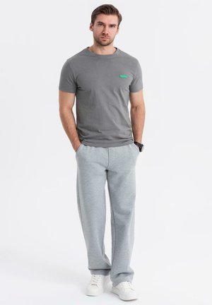 Grå t-shirt med kort ärm och en grön logotyp, tillsammans med ljusgråa sweatpants och vita sneakers, vilket skapar en avslappnad outfit.