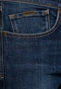Dark blue denim jeans featuring a back pocket with a stitched design and a small tag that reads "Pepe Jeans." Clean texture with contrasting stitching.