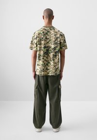 Short-sleeve, camouflage-patterned shirt in beige, green, and black. Paired with loose-fit, olive green cargo pants featuring side pockets.