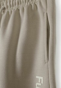 Beige jogger pants made of textured fabric, featuring an elastic waistband and side pockets, with a white logo accent.