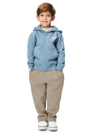 Hellblaue Zip-Hoodie mit einer Vorderentasche, kombiniert mit beigefarbenen Jogginghosen. Verfügt über ein Logo auf der Brust und weiße Turnschuhe.