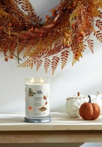Yankee Candle i en klar glasburk med höstiga illustrationer; placerad bredvid en texturerad vit pumpa och en liten orange pumpa.