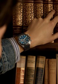 Silver stainless steel chronograph watch with blue face and black leather strap, displaying subdials and contrasting white accents.