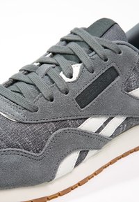 Baskets en suède et mesh gris avec des lacets assortis, des bandes blanches sur le côté et une semelle en caoutchouc marron clair.