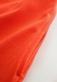 Gros plan sur un tissu orange vif avec des coutures visibles le long du bord, mettant en valeur la texture et les détails des coutures.