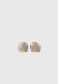 Bailarinas en tejido metálico beige con una textura suave, que cuentan con un acento decorativo atado en la parte posterior y una suela plana y ligera.