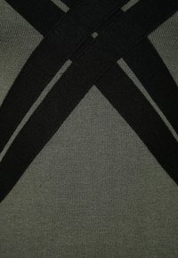 Svart och mörkgrön elastisk tyg med sammansydda remmar som skapar ett korsmönster. Slät textur med fint stickad detaljer.