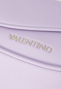 Ljubičasta kožna torba s glatkom teksturom, koja se odlikuje uzdignutim metalik logotipom "VALENTINO" sprijeda i diskretnim detaljima šivanja.