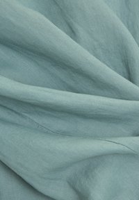 Tissu en lin bleu clair avec une texture douce, présentant des plis légers et une apparence lisse, affichant un éclat subtil par endroits.