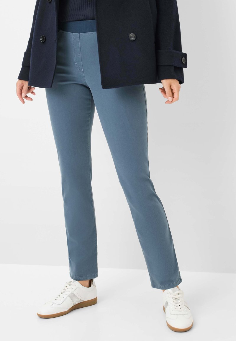 Pantaloni elastici blu con vita media, abbinati a sneaker bianche. I pantaloni presentano una vestibilità slim e una texture di tessuto liscia.