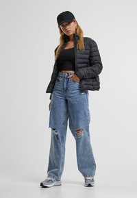 Doudoune noire, haut noir cropped, jeans déchirés taille haute bleu clair, casquette noire et baskets grises. Tenue décontractée avec des textures variées.