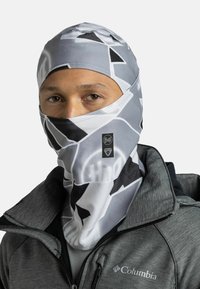 Buff balaclava in a gray and white geometric pattern, made of soft, stretchy fabric. Worn over the face, paired with a gray jacket.