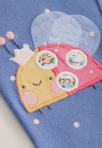 Motif brodé d'une coccinelle dessin animé en jaune et rouge sur fond bleu, avec des visages circulaires et des accents roses. Tissu texturé.