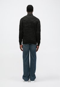 Pulover negru texturat cu un design cu modele, asortat cu blugi lejeri din denim albastru și teniși albi, văzut din spate.