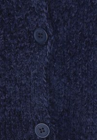 Granatowy sweter z dzianiny z teksturowanym splotem i dwoma okrągłymi guzikami w ciemnoniebieskim odcieniu, podkreślający ciepło i zróżnicowany design.