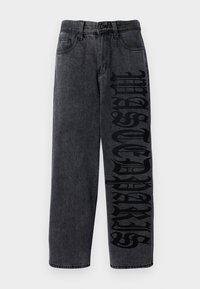 Must värvi denim püksid, millel on avar lõige, suurte stiliseeritud mustade kirjadega vasakul jalal ja tavaline viie taskuga disain.