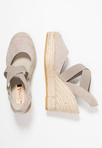 Béžové semišové espadrilky na klínu se splétanou jutu, elastickými křížovými popruhy a kulatou špičkou. Texturovaný svršek doplňuje tkané detaily.