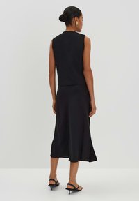 Schwarzes ärmelloses Top kombiniert mit einem passenden knielangen Rock, der über eine glatte Textur und einen seitlichen Schlitz verfügt, getragen mit schwarzen Riemchensandalen.