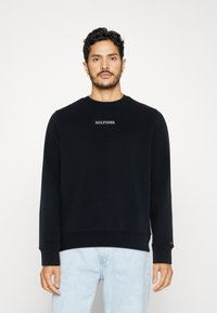 Felpa nera con colletto a girocollo realizzata in cotone, caratterizzata da un piccolo logo ricamato sul petto, polsini a coste e una vestibilità rilassata.