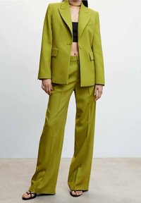 Blazer ajustado de color verde lima con pantalones de pierna ancha a juego, que presenta un cierre de un solo botón, solapas afiladas y bolsillos frontales. Lleva puesto un top corto negro.