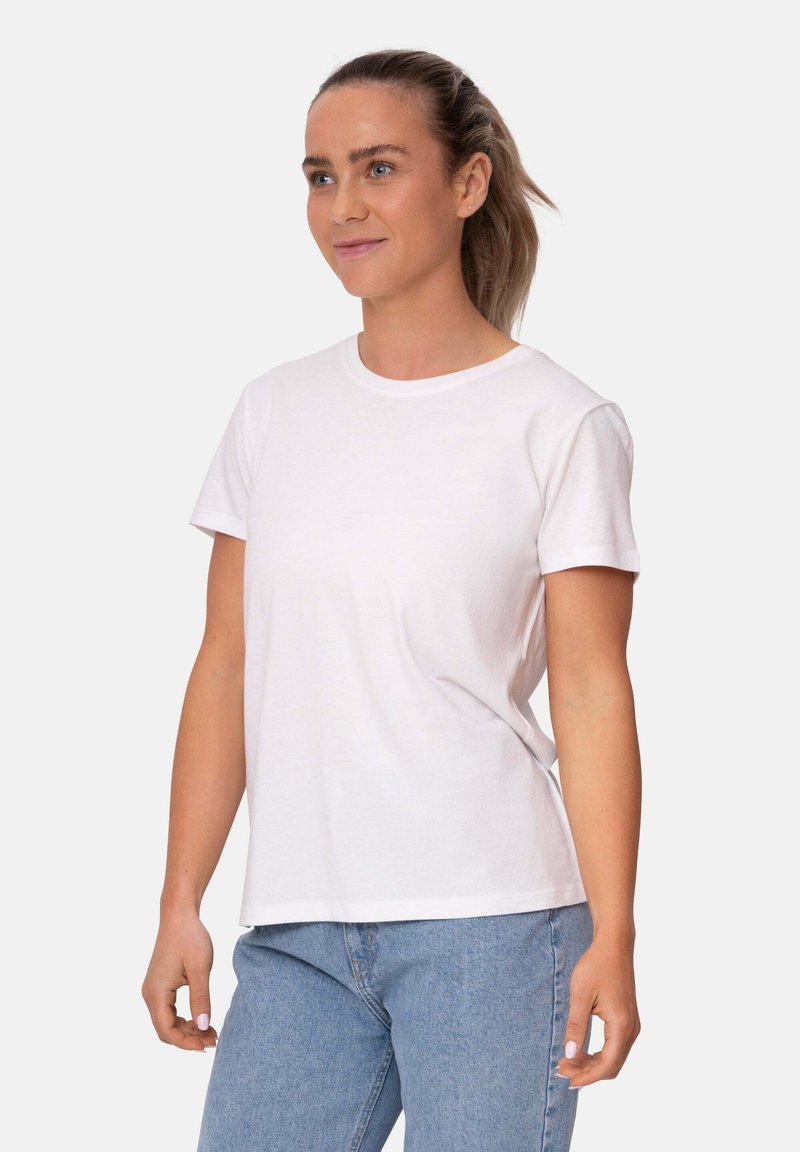 Camiseta de algodón blanca de manga corta y cuello redondo, con un ajuste relajado y textura suave. Lleva puesta con jeans de color azul claro.