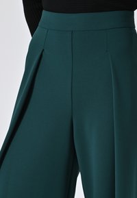 Wijdbeense teal broek met geplooide details bij de taille. Gemaakt van een gladde stof met een matte afwerking.