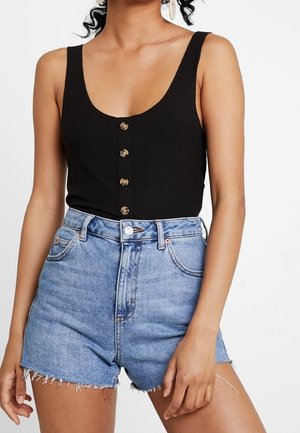 Vrouw draagt een zwart mouwloos topje met knopen en lichtblauwe denim shorts met hoge taille en rafelige zoom.