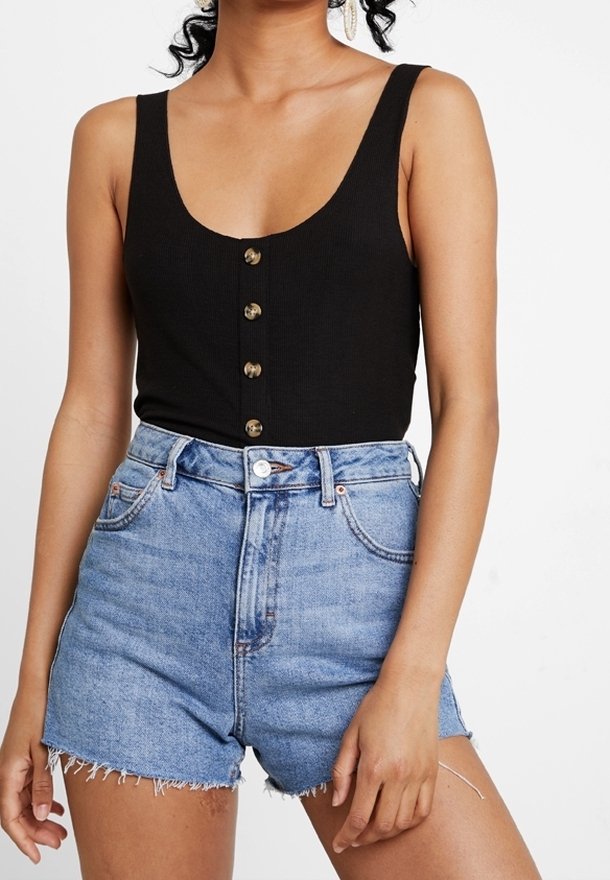 Femme portant un haut noir sans manches à boutons et un short en denim bleu clair taille haute avec des ourlets effilochés.