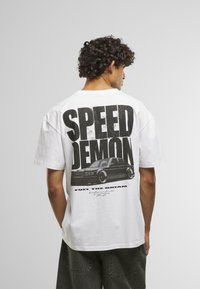 White cotton T-shirt featuring a large black graphic print on the back with the words "SPEED DEMON" and an illustration of a car.