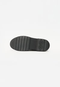Semelle de chaussure en caoutchouc noir avec des nervures horizontaless, un logo près du talon et une surface texturée pour l'adhérence.
